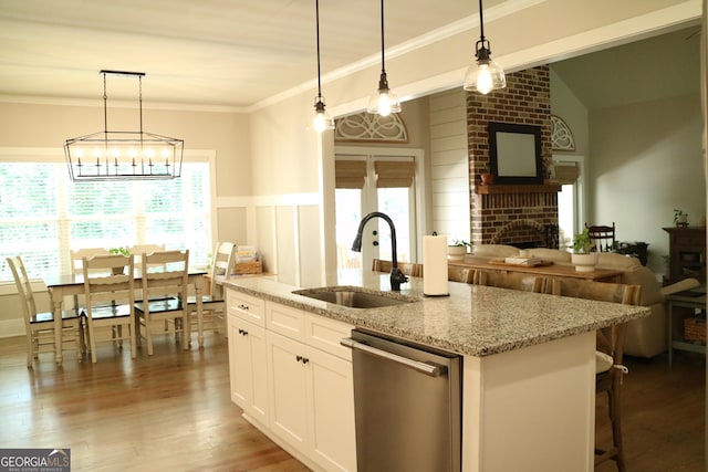 kitchen with open floor plan, white cabinets, a sink, light stone countertops, and dishwasher