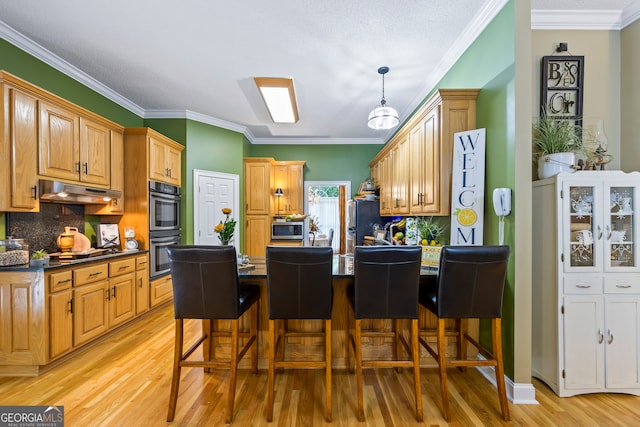 kitchen featuring under cabinet range hood, double wall oven, a peninsula, stainless steel microwave, and dark countertops