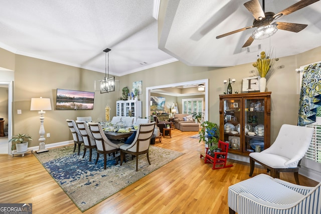 dining area with a textured ceiling, ceiling fan with notable chandelier, wood finished floors, baseboards, and ornamental molding