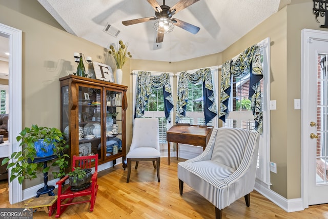 living area with a ceiling fan, a wealth of natural light, visible vents, and wood finished floors