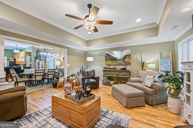 living room with light wood-style flooring, ceiling fan with notable chandelier, visible vents, ornamental molding, and a raised ceiling