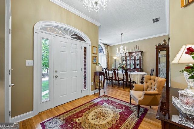 entrance foyer featuring a chandelier, ornamental molding, wood finished floors, and visible vents