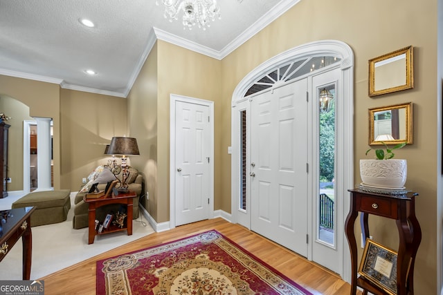 foyer entrance with light wood finished floors, baseboards, arched walkways, ornamental molding, and a notable chandelier