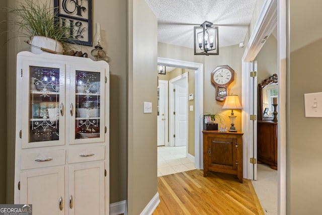 hallway with a textured ceiling, baseboards, light wood-style flooring, and an inviting chandelier