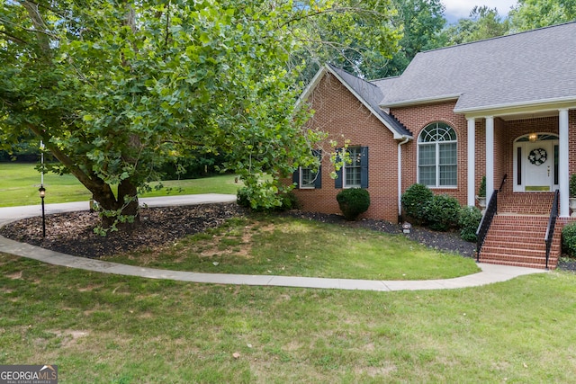 view of front of property featuring a front yard, brick siding, and roof with shingles