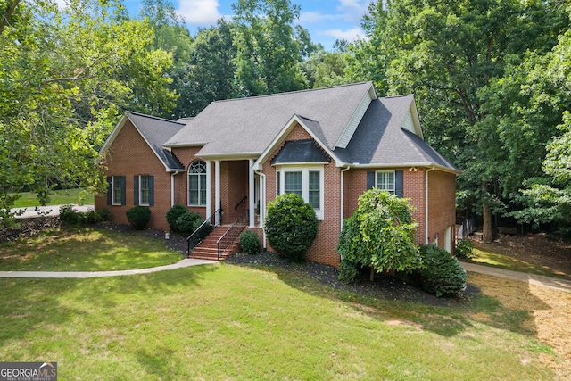 view of front facade with brick siding, a shingled roof, and a front yard