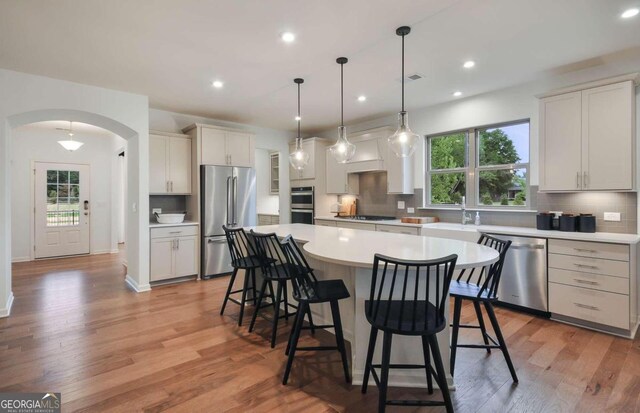 kitchen featuring appliances with stainless steel finishes, white cabinetry, hanging light fixtures, light wood-type flooring, and a spacious island