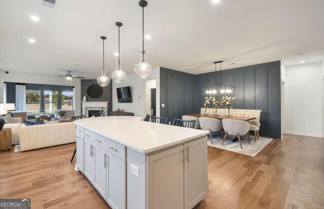 kitchen with white cabinetry, hanging light fixtures, light hardwood / wood-style floors, a kitchen island, and ceiling fan with notable chandelier