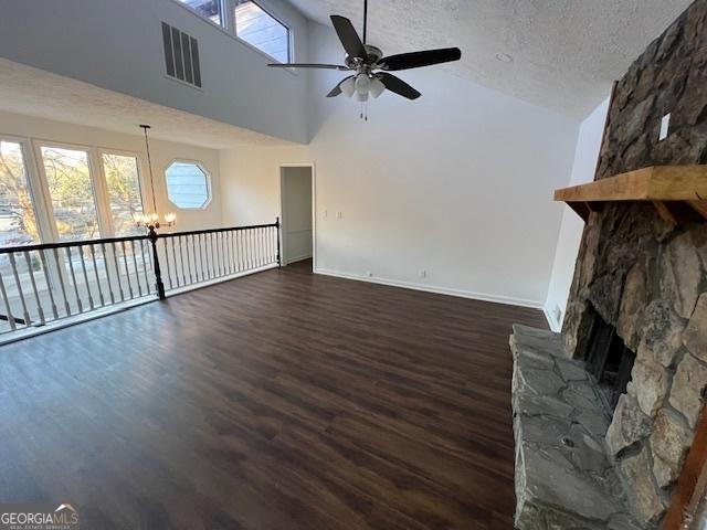 unfurnished living room featuring dark hardwood / wood-style flooring, high vaulted ceiling, a textured ceiling, a fireplace, and ceiling fan with notable chandelier