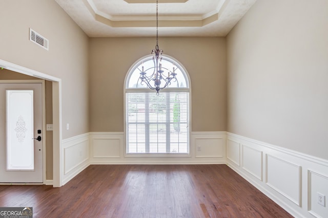 unfurnished dining area featuring a raised ceiling, crown molding, dark wood-type flooring, and an inviting chandelier