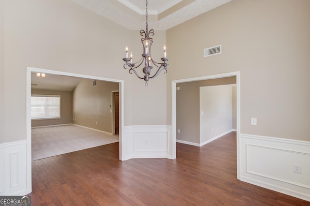 unfurnished dining area featuring a notable chandelier, dark wood-type flooring, and a raised ceiling