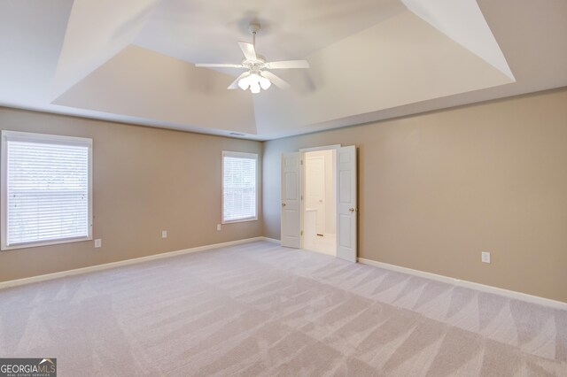 unfurnished bedroom featuring multiple windows, light carpet, a raised ceiling, and ceiling fan