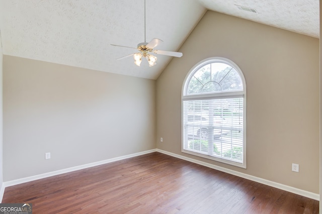 empty room with hardwood / wood-style flooring, vaulted ceiling, plenty of natural light, and a textured ceiling