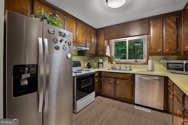 kitchen featuring stainless steel appliances, light hardwood / wood-style floors, sink, and a textured ceiling