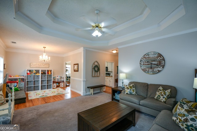 living area with ceiling fan with notable chandelier, ornamental molding, visible vents, wood finished floors, and a raised ceiling