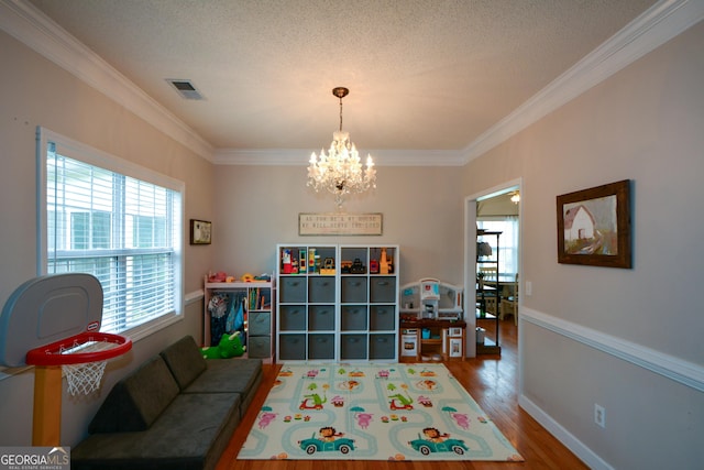 playroom featuring ornamental molding, a chandelier, a textured ceiling, visible vents, and wood finished floors