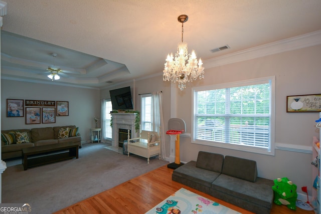 living room with ornamental molding, a fireplace with flush hearth, visible vents, ceiling fan with notable chandelier, and wood finished floors