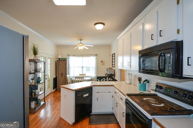kitchen with white cabinets, a peninsula, light wood-type flooring, and black appliances