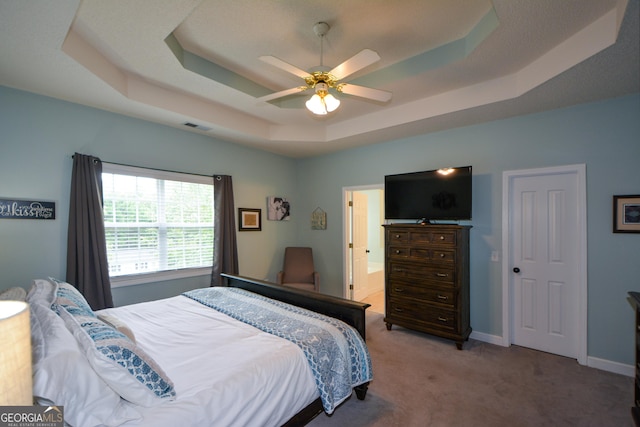 bedroom featuring baseboards, visible vents, a tray ceiling, ceiling fan, and light colored carpet