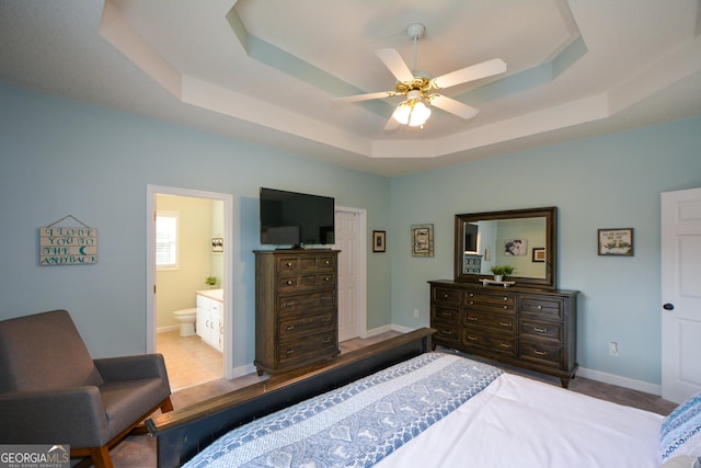 bedroom featuring ensuite bathroom, a tray ceiling, and ceiling fan