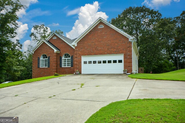 traditional-style home featuring an attached garage, concrete driveway, a front yard, and brick siding