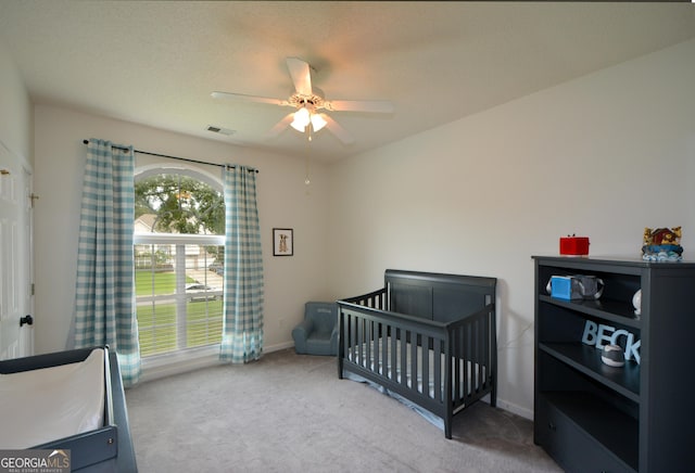 carpeted bedroom with ceiling fan, baseboards, visible vents, and a crib