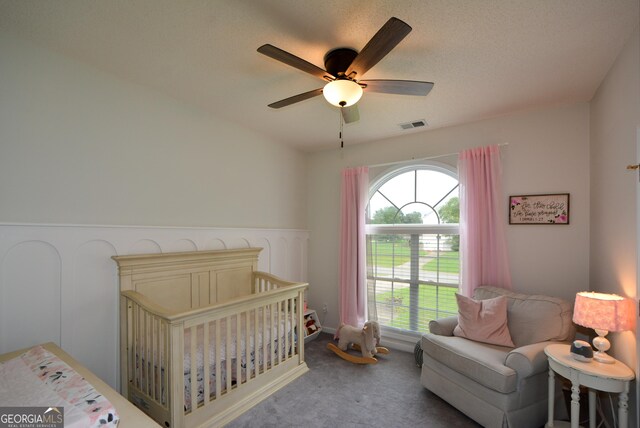 carpeted bedroom featuring visible vents, a ceiling fan, and a crib