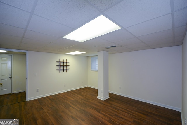 finished below grade area with visible vents, baseboards, a drop ceiling, and wood finished floors
