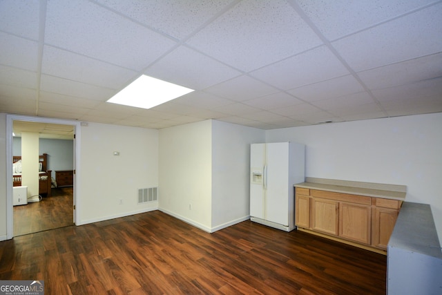 basement with dark wood-type flooring, visible vents, a paneled ceiling, and white fridge with ice dispenser