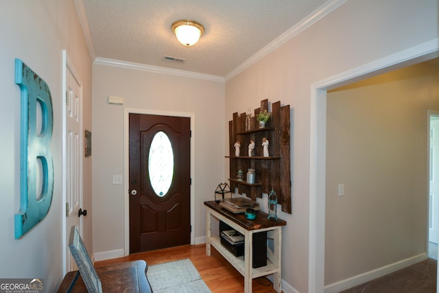 entryway featuring baseboards, ornamental molding, a textured ceiling, visible vents, and wood finished floors