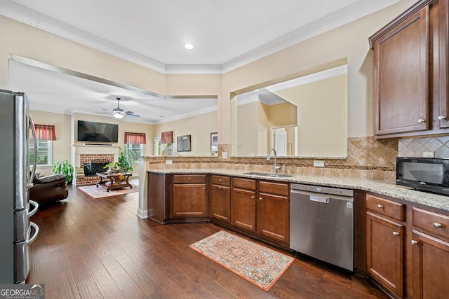 kitchen featuring a brick fireplace, light stone countertops, stainless steel appliances, dark wood-type flooring, and sink