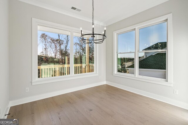 unfurnished dining area with wood-type flooring, an inviting chandelier, and crown molding