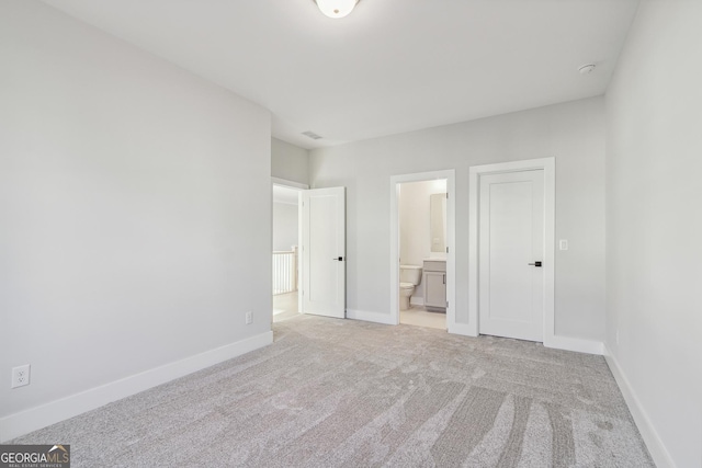 unfurnished bedroom with ensuite bathroom and light colored carpet