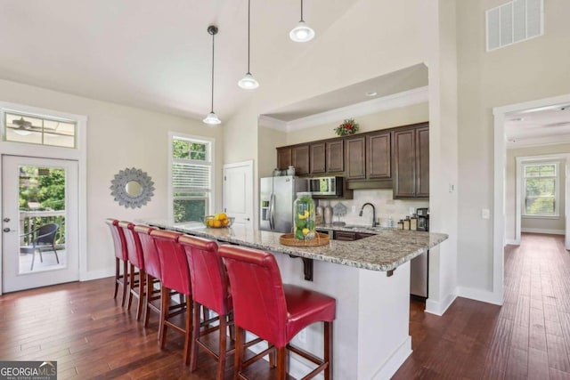 kitchen with dark brown cabinetry, hanging light fixtures, light stone counters, a breakfast bar, and appliances with stainless steel finishes