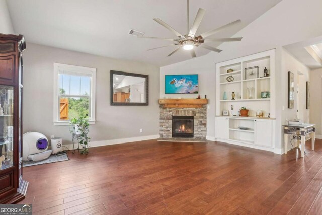 living room with built in shelves, ceiling fan, a stone fireplace, dark hardwood / wood-style floors, and vaulted ceiling