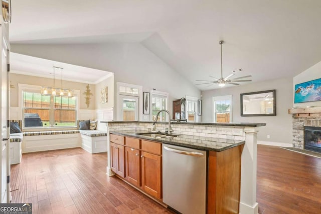 kitchen with sink, stainless steel dishwasher, an island with sink, decorative light fixtures, and a fireplace