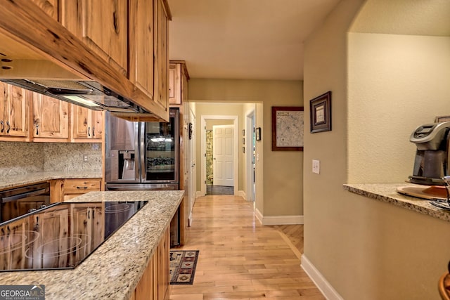 kitchen with black electric stovetop, premium range hood, decorative backsplash, light wood-type flooring, and light stone counters