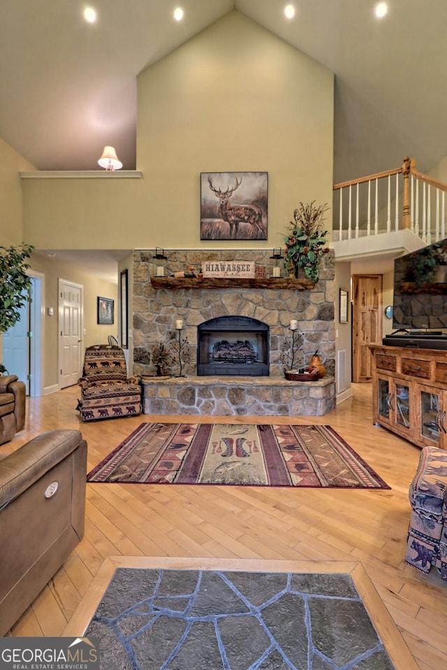 living room featuring light hardwood / wood-style flooring, a stone fireplace, and high vaulted ceiling