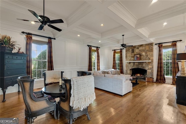 dining room with crown molding, wood-type flooring, a stone fireplace, and beamed ceiling