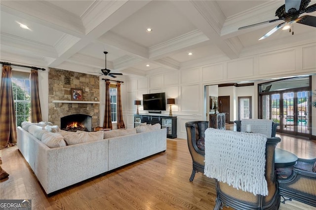 living room featuring light hardwood / wood-style floors, coffered ceiling, a fireplace, crown molding, and beam ceiling