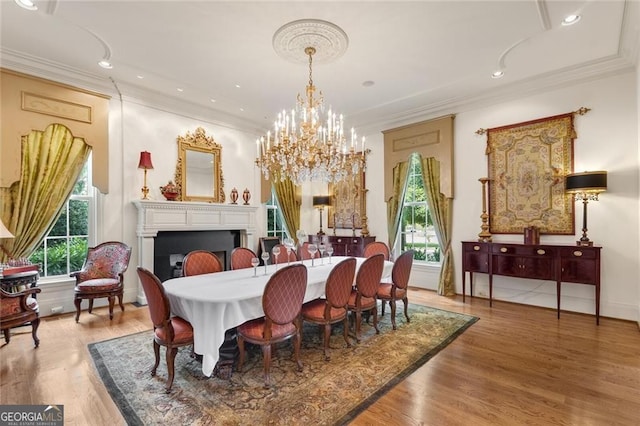 dining space with a healthy amount of sunlight, wood-type flooring, an inviting chandelier, and crown molding