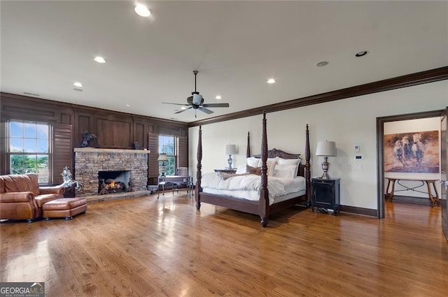 bedroom with ceiling fan, a stone fireplace, ornamental molding, and hardwood / wood-style floors