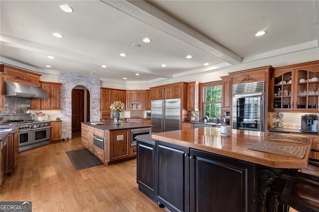 kitchen featuring wall chimney range hood, a center island, beam ceiling, and built in appliances