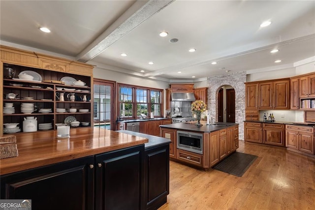 kitchen featuring wall chimney range hood, a kitchen island, beamed ceiling, appliances with stainless steel finishes, and butcher block counters