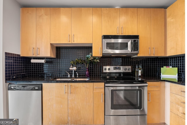 kitchen with stainless steel appliances, sink, decorative backsplash, and dark stone counters