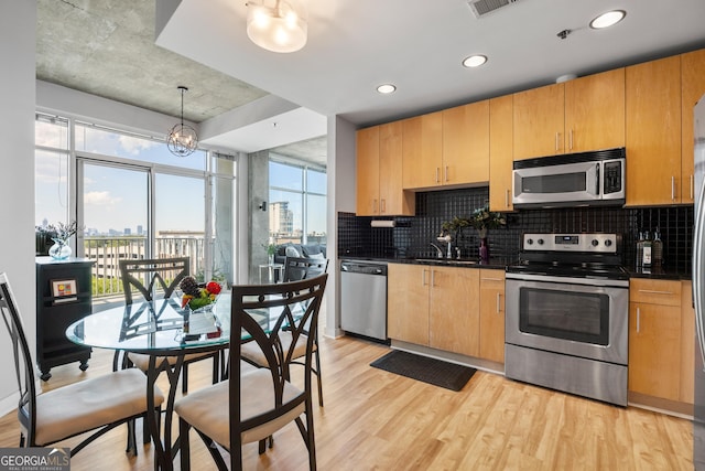 kitchen featuring tasteful backsplash, appliances with stainless steel finishes, decorative light fixtures, and light wood-type flooring