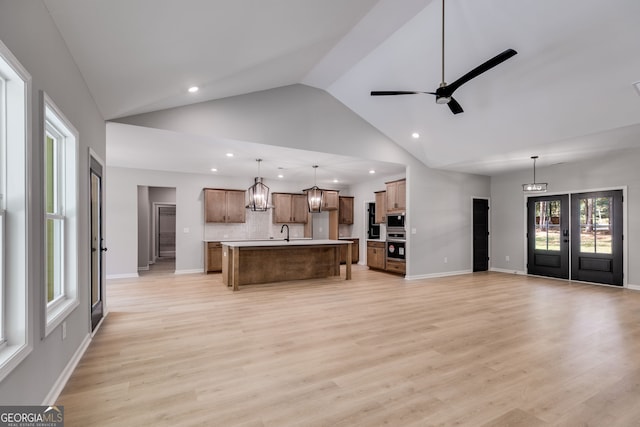 living room featuring light hardwood / wood-style flooring, high vaulted ceiling, ceiling fan with notable chandelier, and plenty of natural light