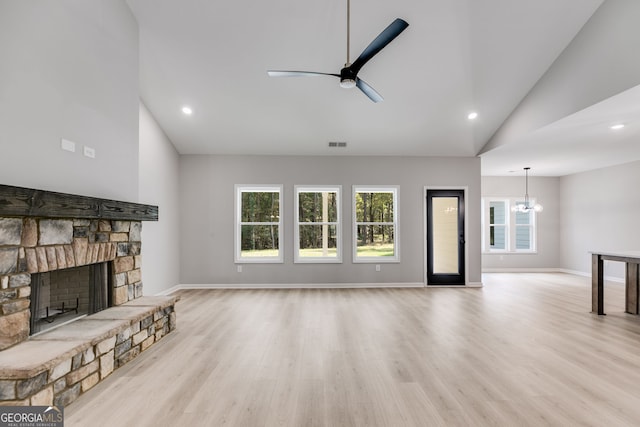 unfurnished living room featuring ceiling fan with notable chandelier, a stone fireplace, high vaulted ceiling, and light wood-type flooring