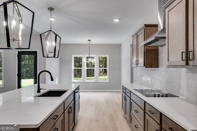 kitchen with black electric stovetop, light hardwood / wood-style flooring, a center island with sink, sink, and light stone counters