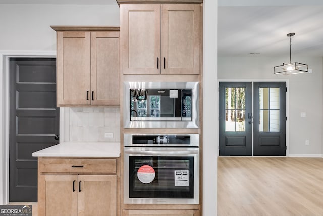 kitchen with light wood-type flooring, stainless steel appliances, pendant lighting, decorative backsplash, and light brown cabinets